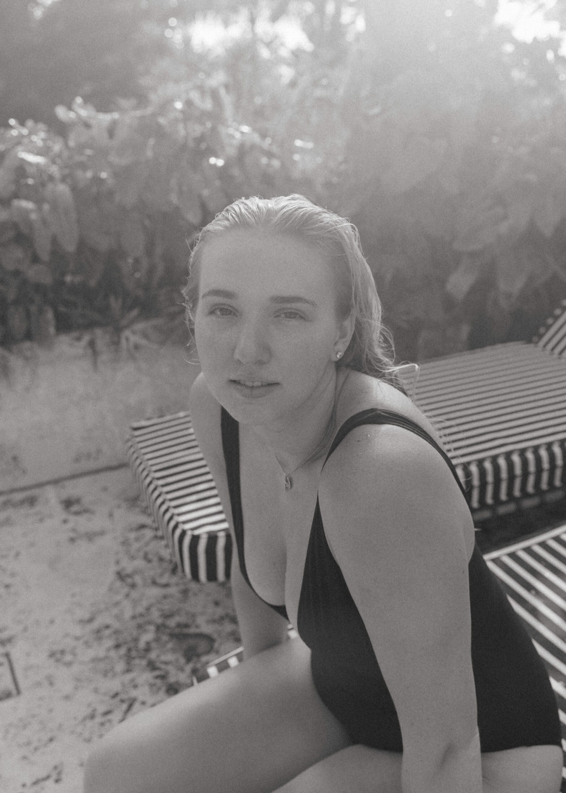 artistic female portrait photography of a woman sitting on a pool chair looking into the camera 