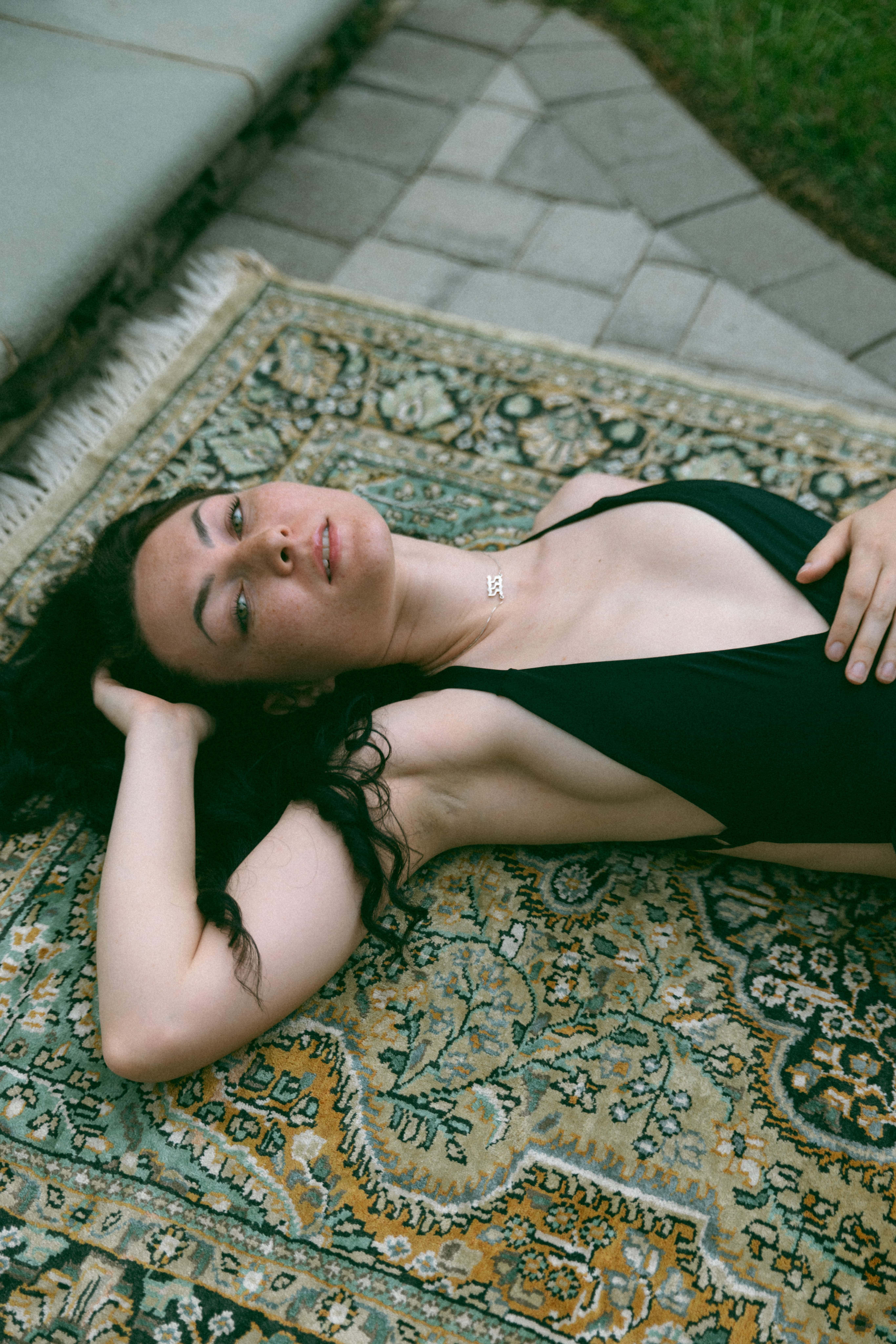a woman in a swimming suit laying on a rug next to the pool 