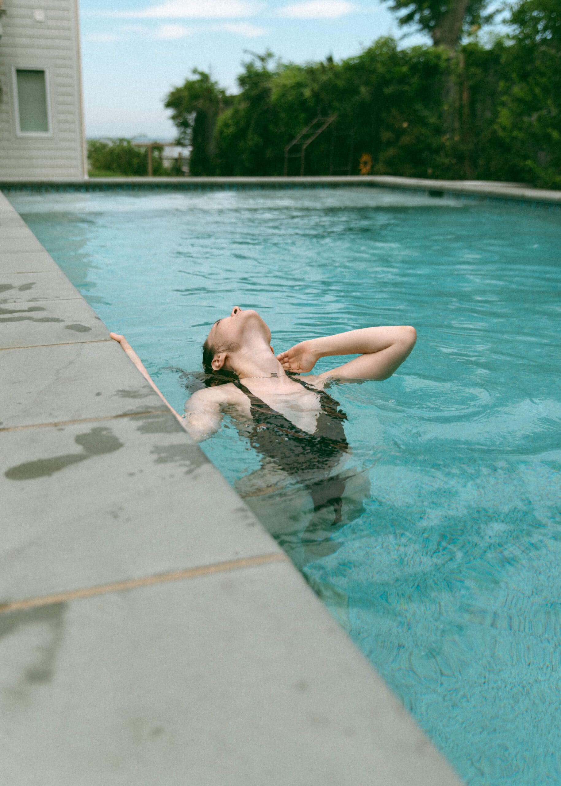 a woman tipping her head back into the pool water during an outdoor boudoir session