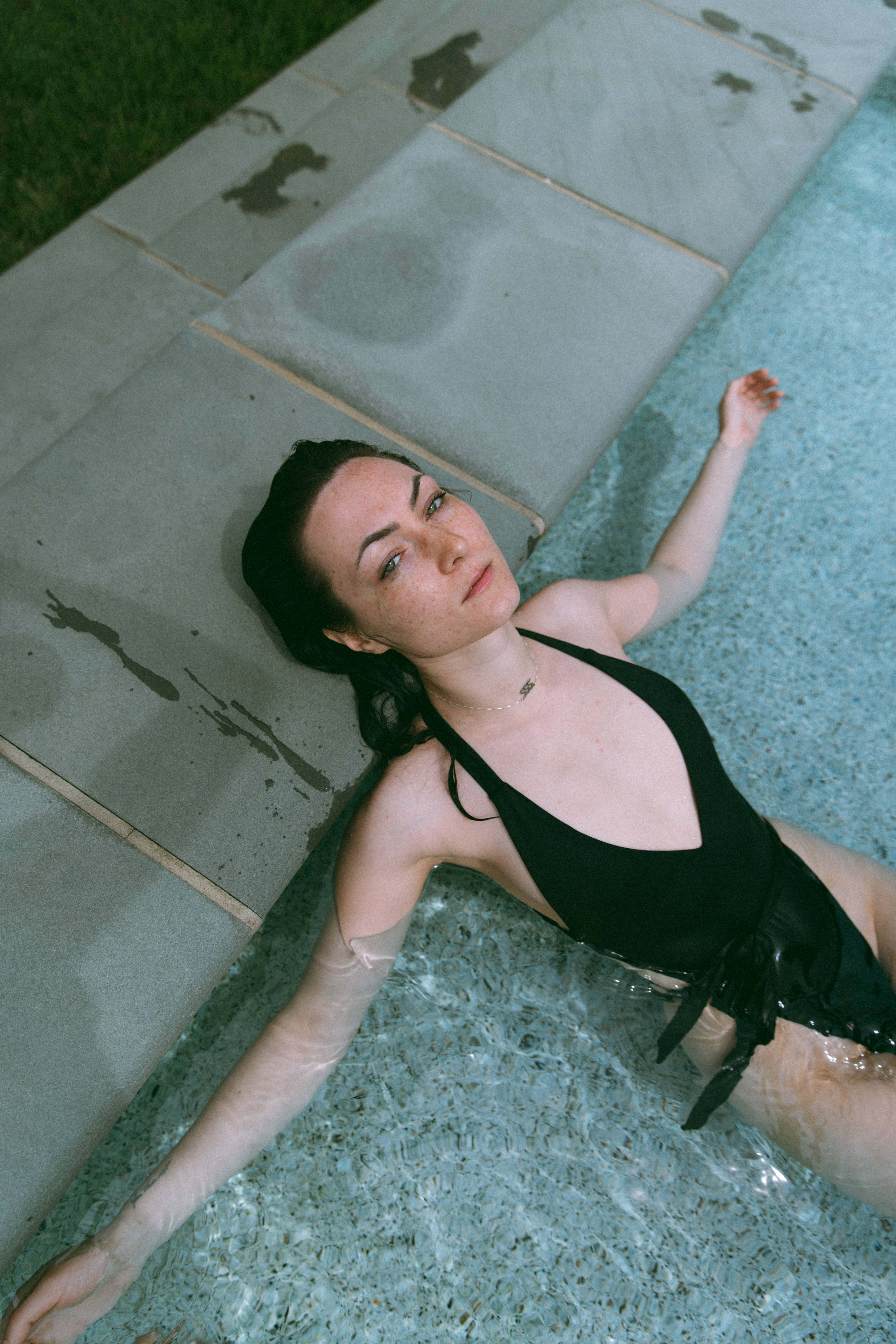 a woman in a pool with her head resting on the edge looking up at the camera