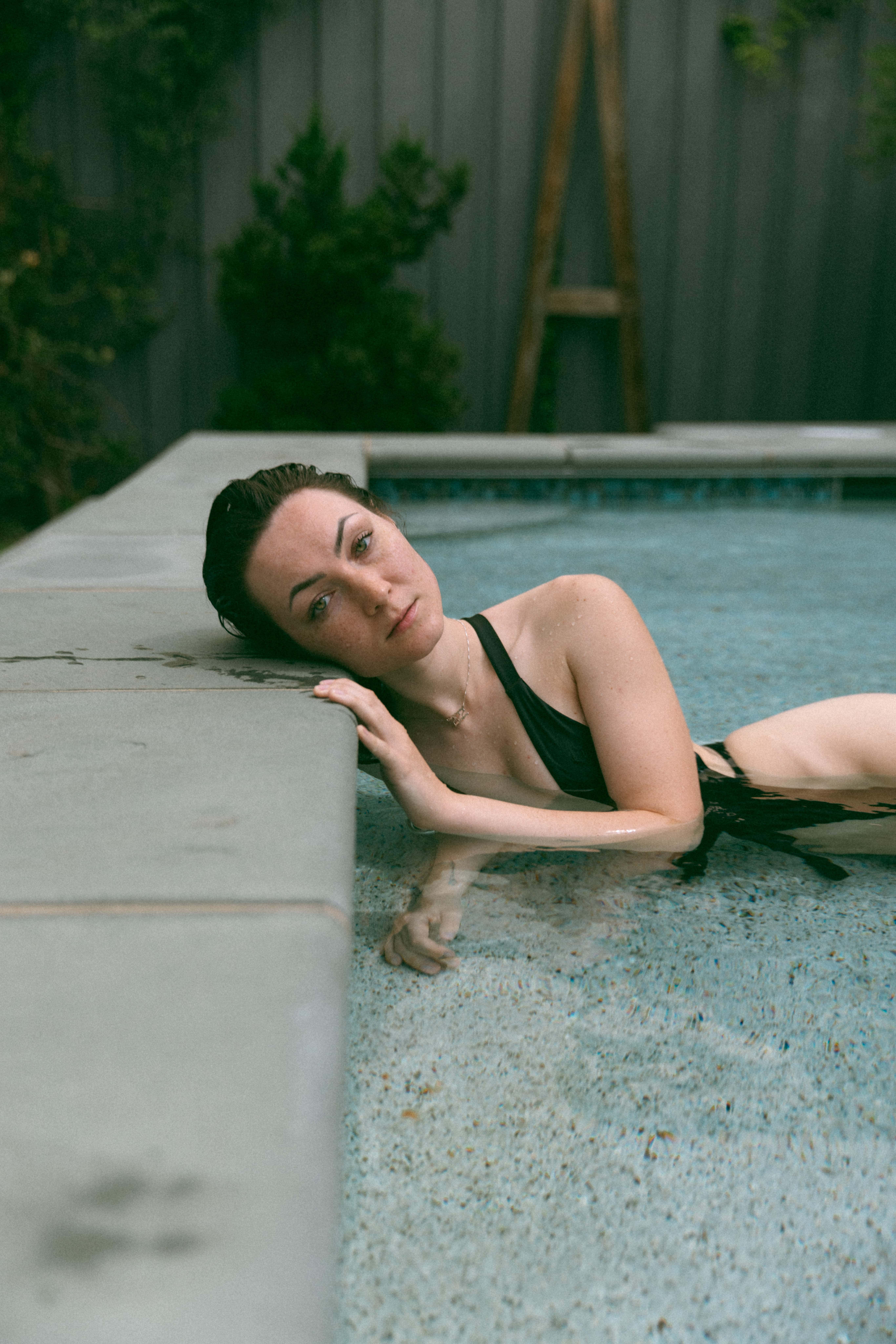 a woman in a swimming pool laying her head on the edge during an outdoor boudoir session