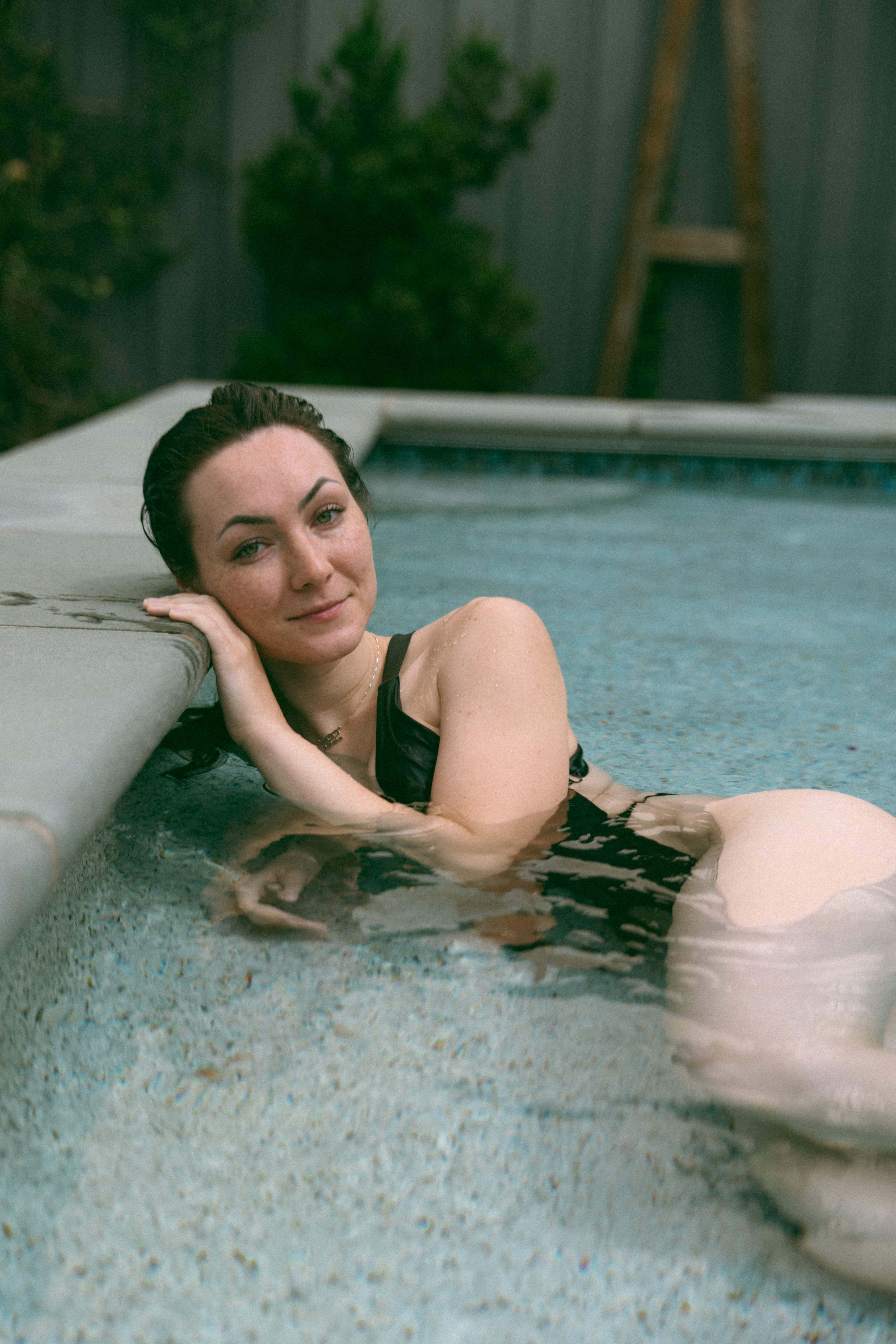 a woman laying in a pool with her head on the edge and smiling at the camera 