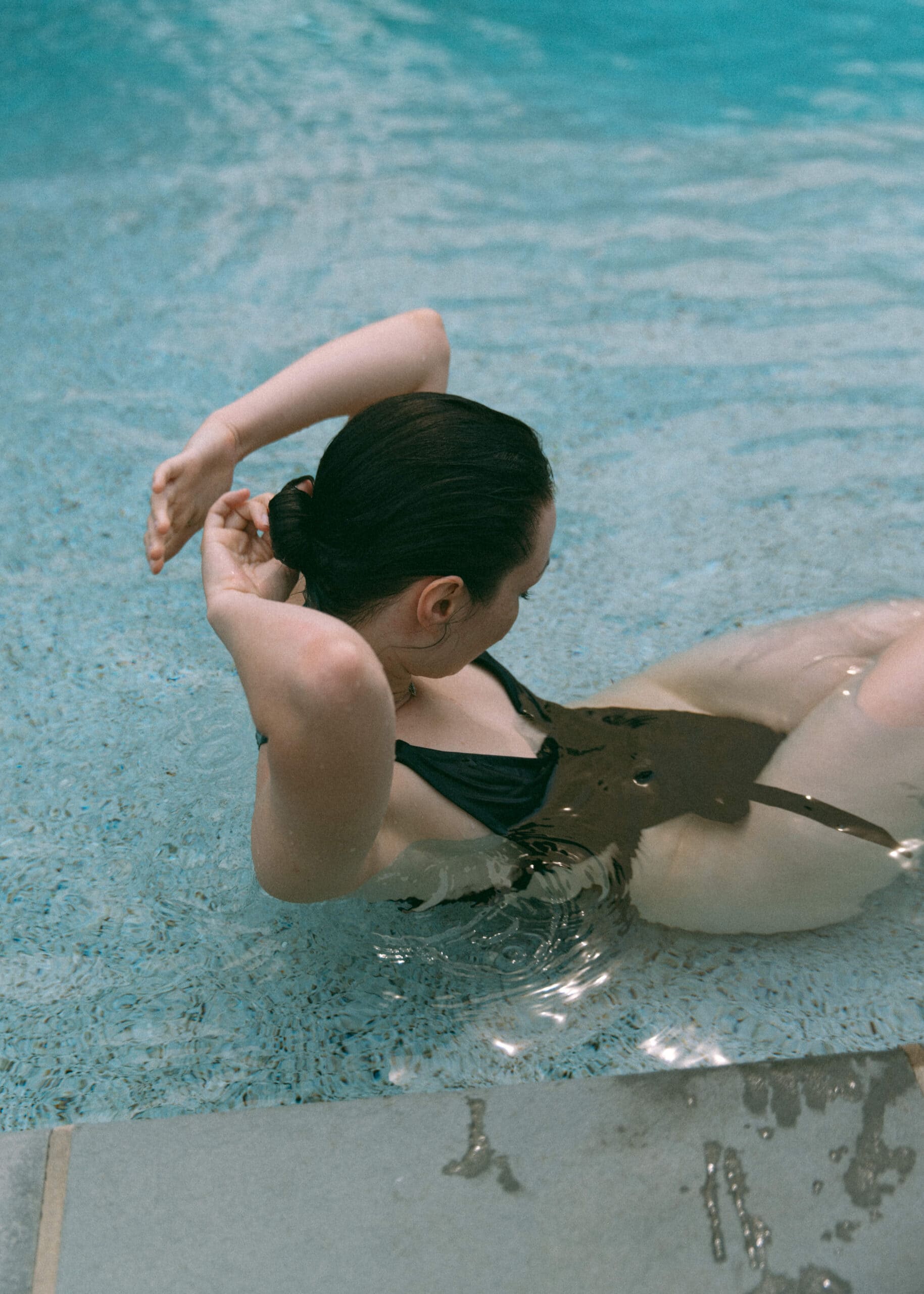 a woman in a pool putting her hair in a pony tail 