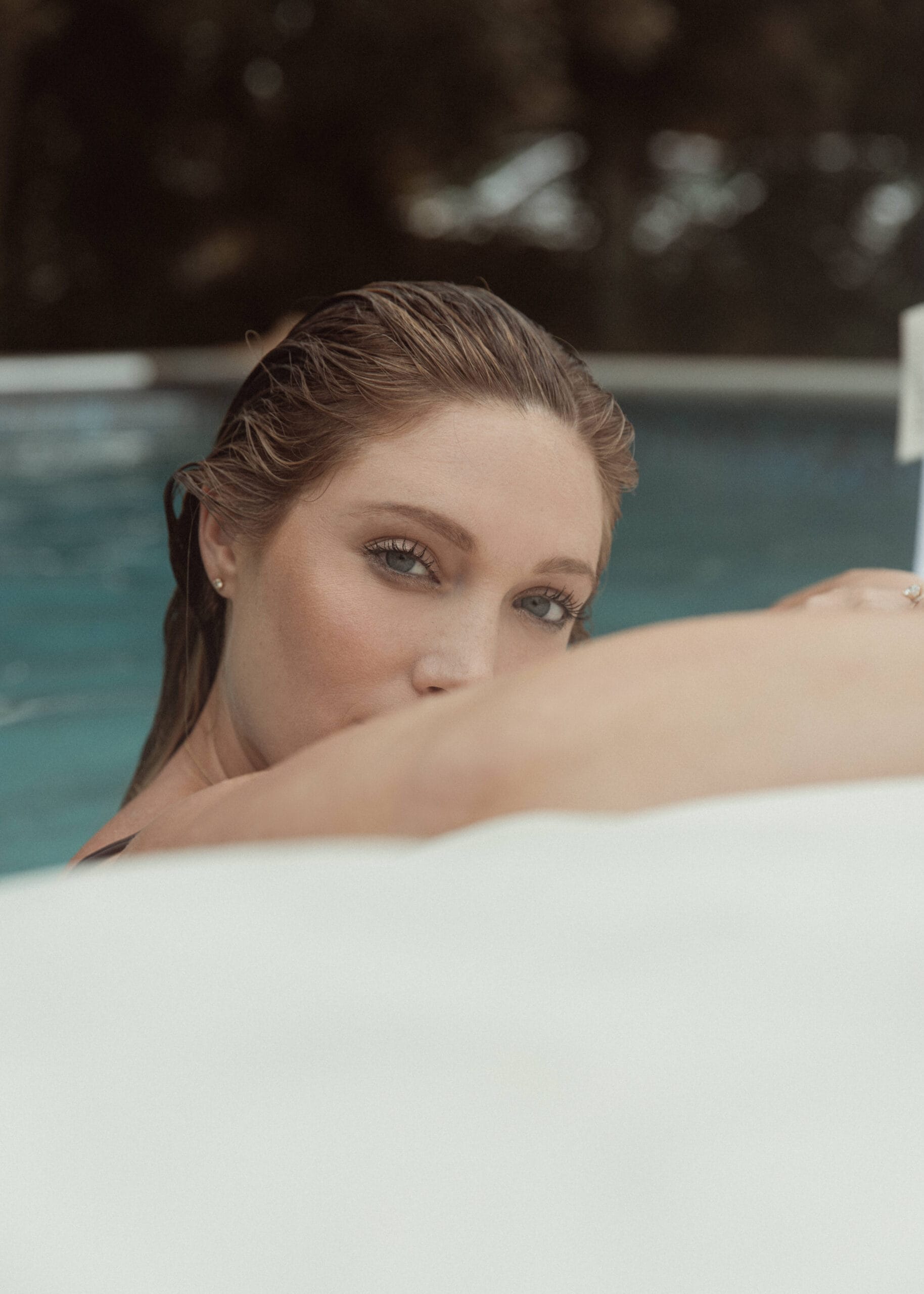a woman looking at the camera from inside the pool during an outdoor boudoir session