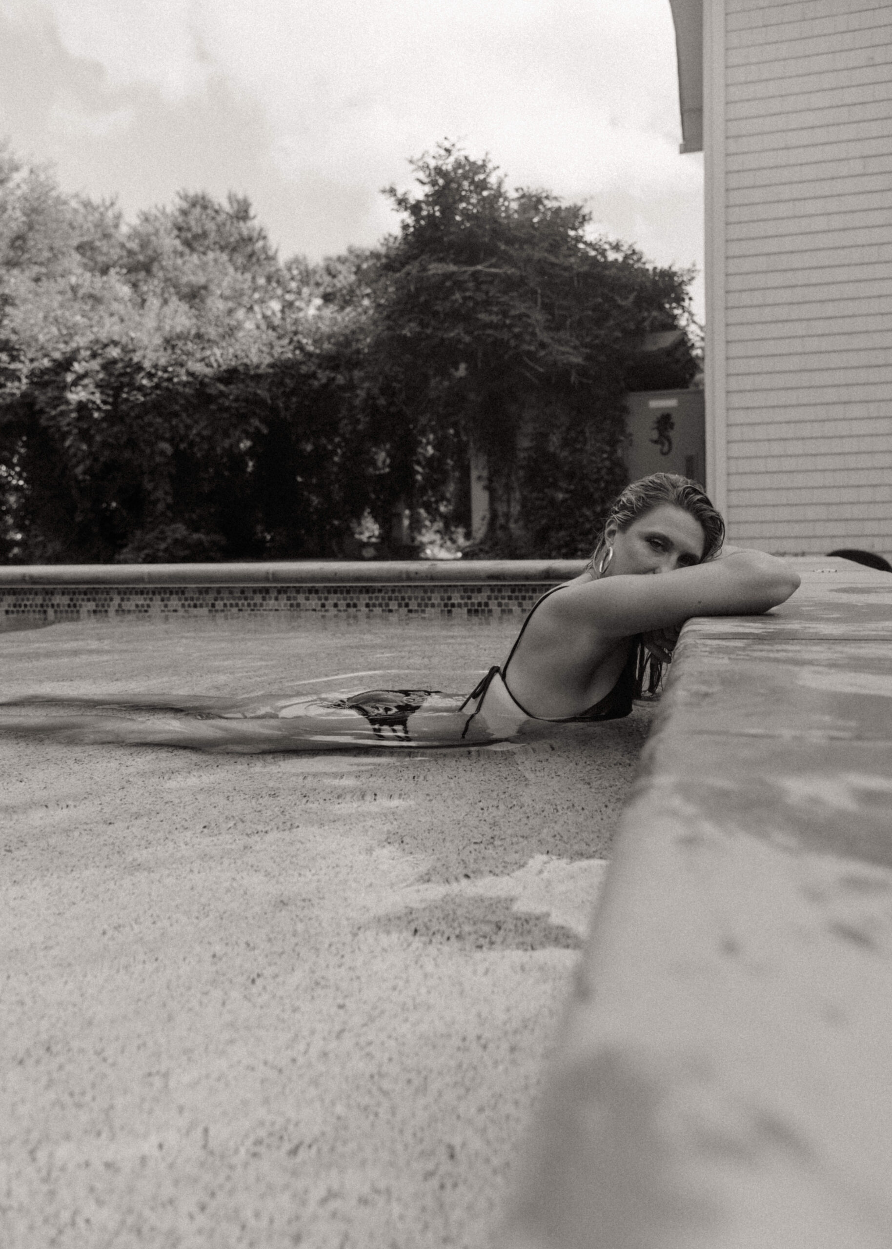 a woman laying in the shallow end of the pool with her head on the edge during an outdoor boudoir session