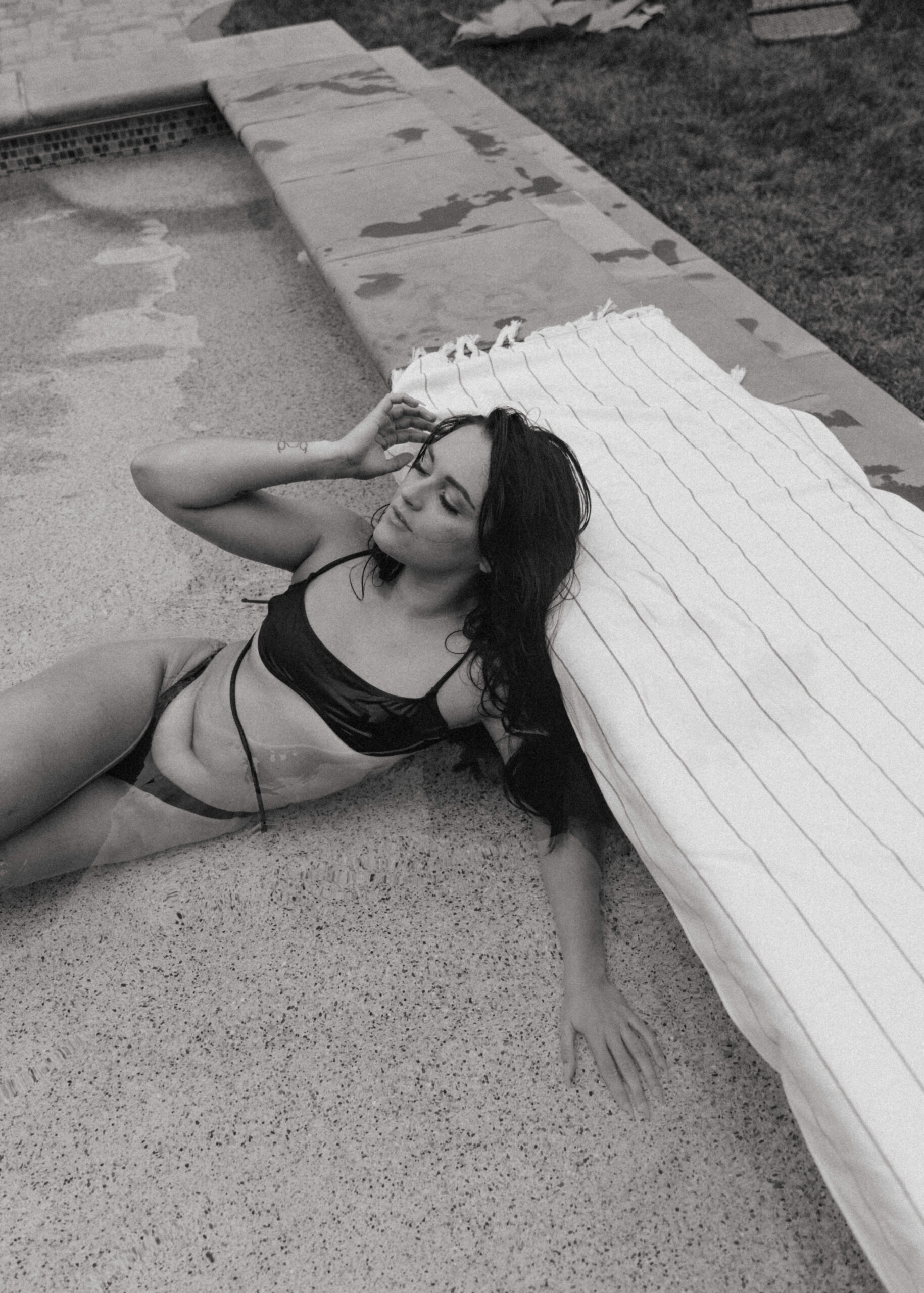 a woman laying in the pool with her head resting on the edge during an outdoor boudoir session