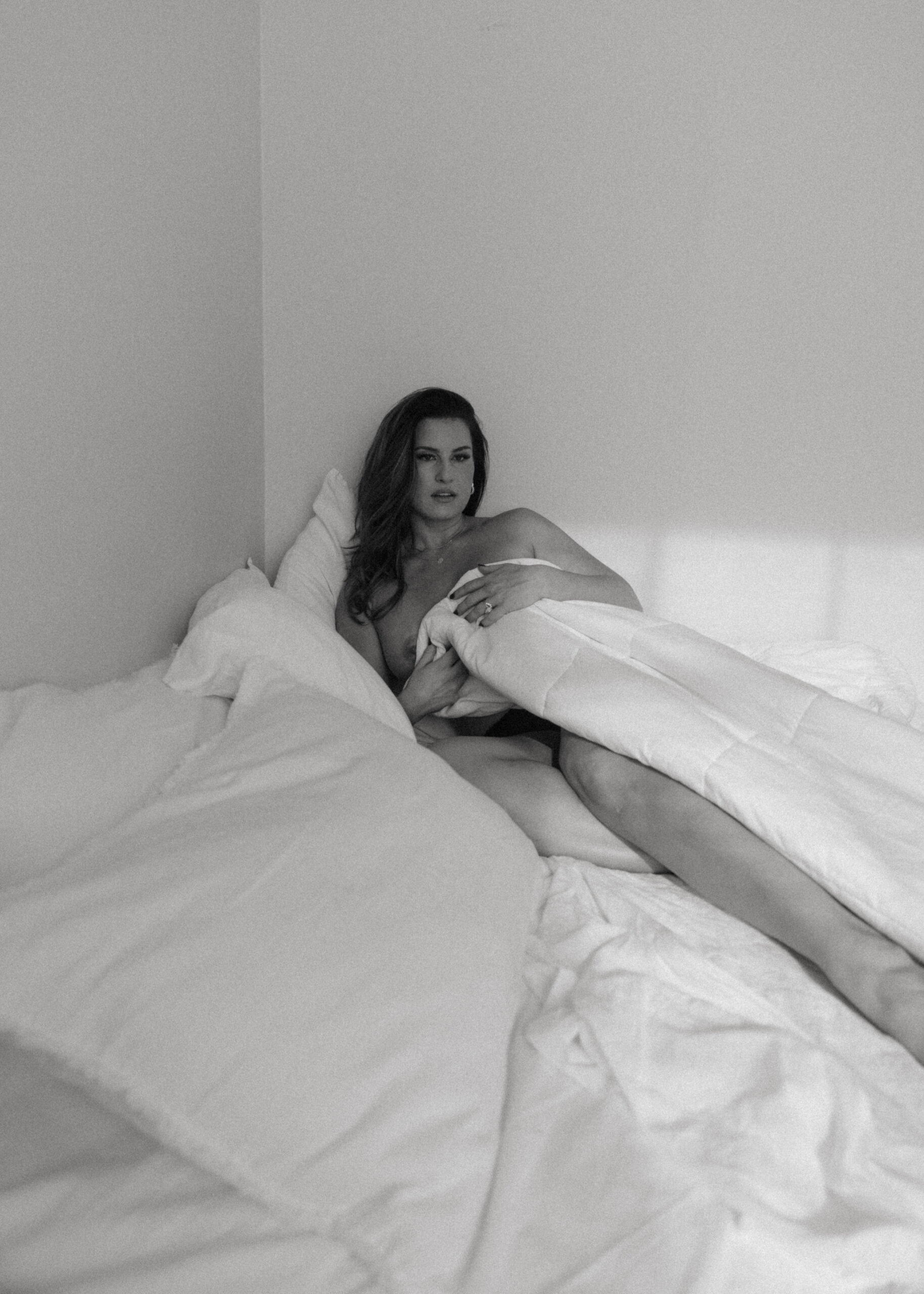 a woman covered up on a bed during a maryland boudoir photography session 