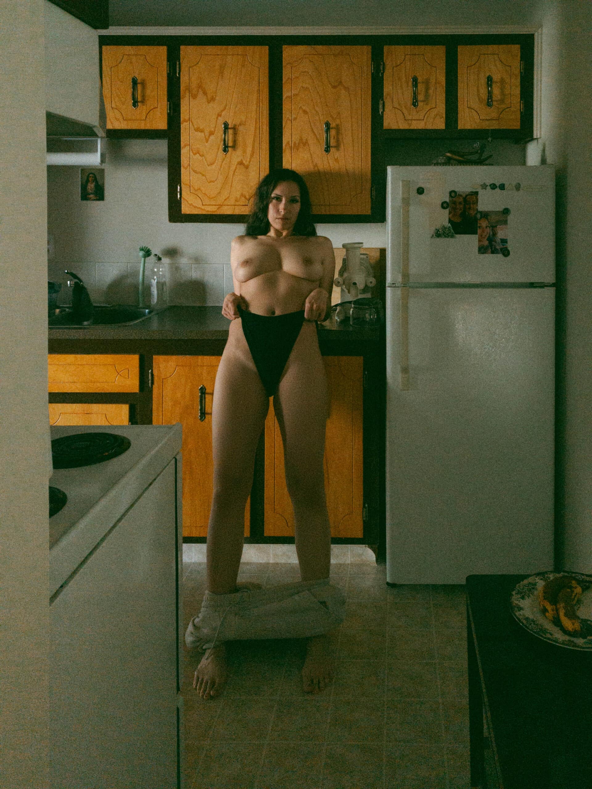 a topless woman leaning back onto her kitchen counter during at home boudoir photos 