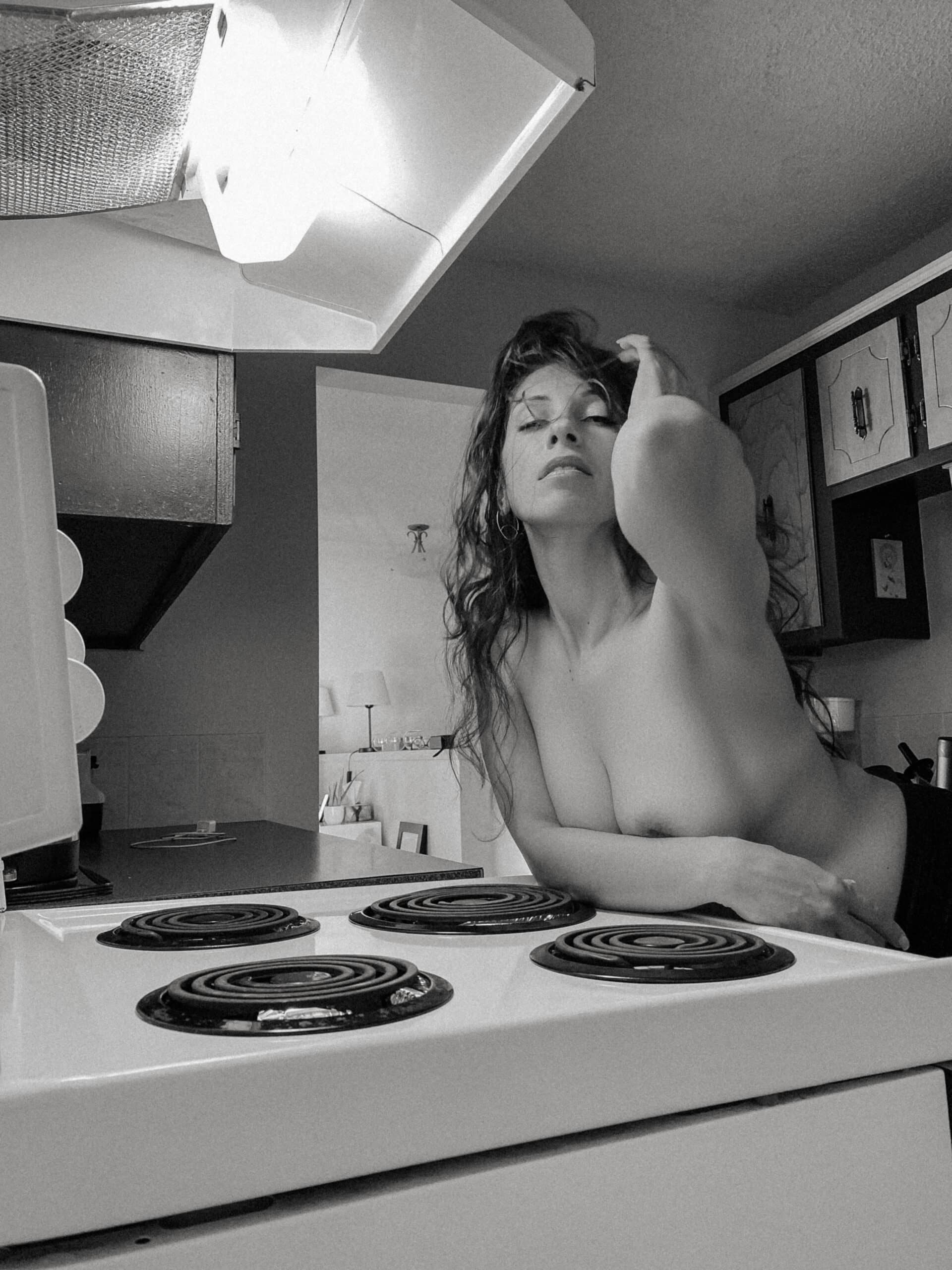 a topless woman by the stove in her kitchen during at home boudoir photos 