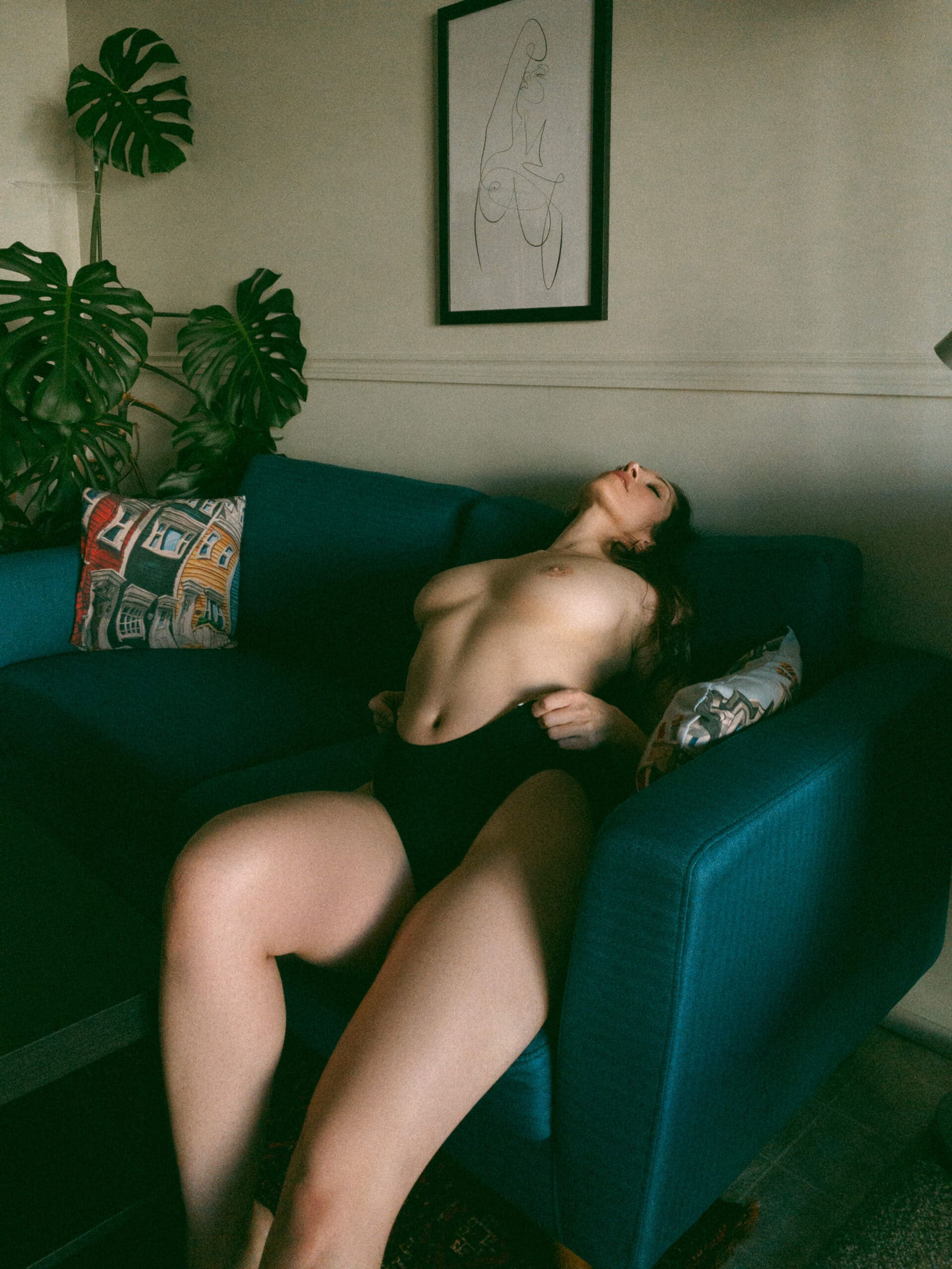 a topless woman leaning back on her couch holding her underwear 