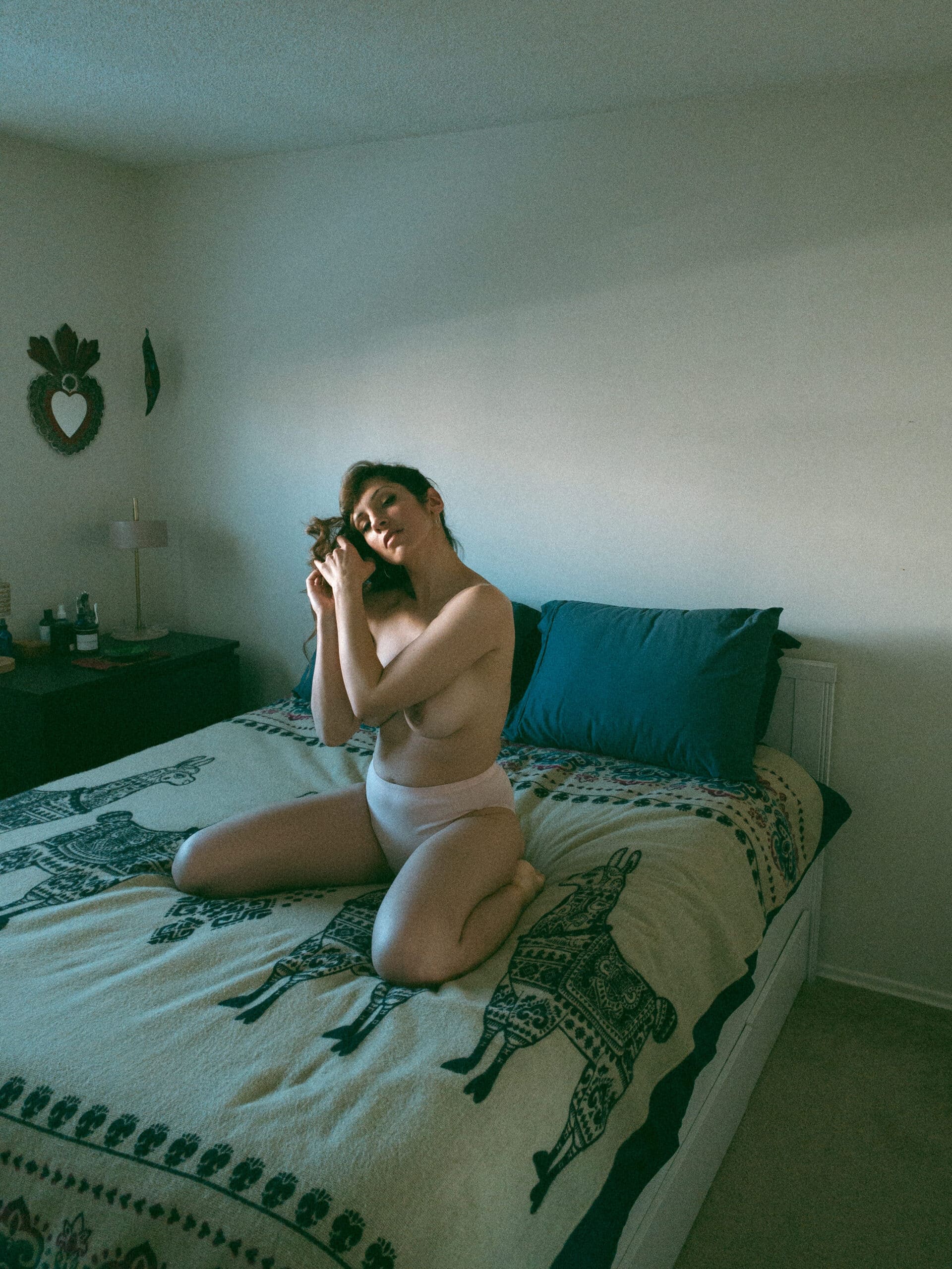 a topless woman sitting on her knees on her bed