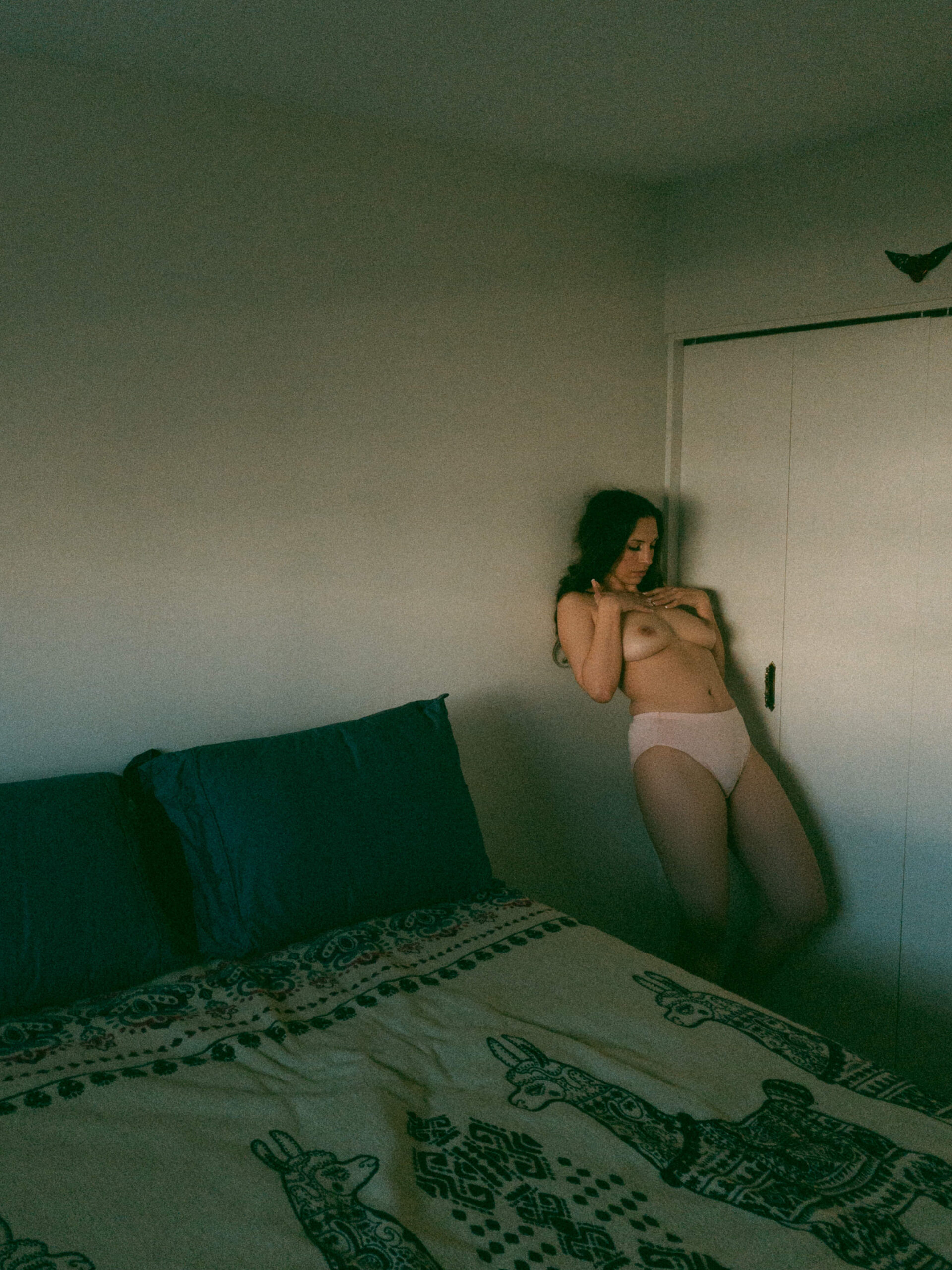a topless woman leaning back against her wall by her bed 