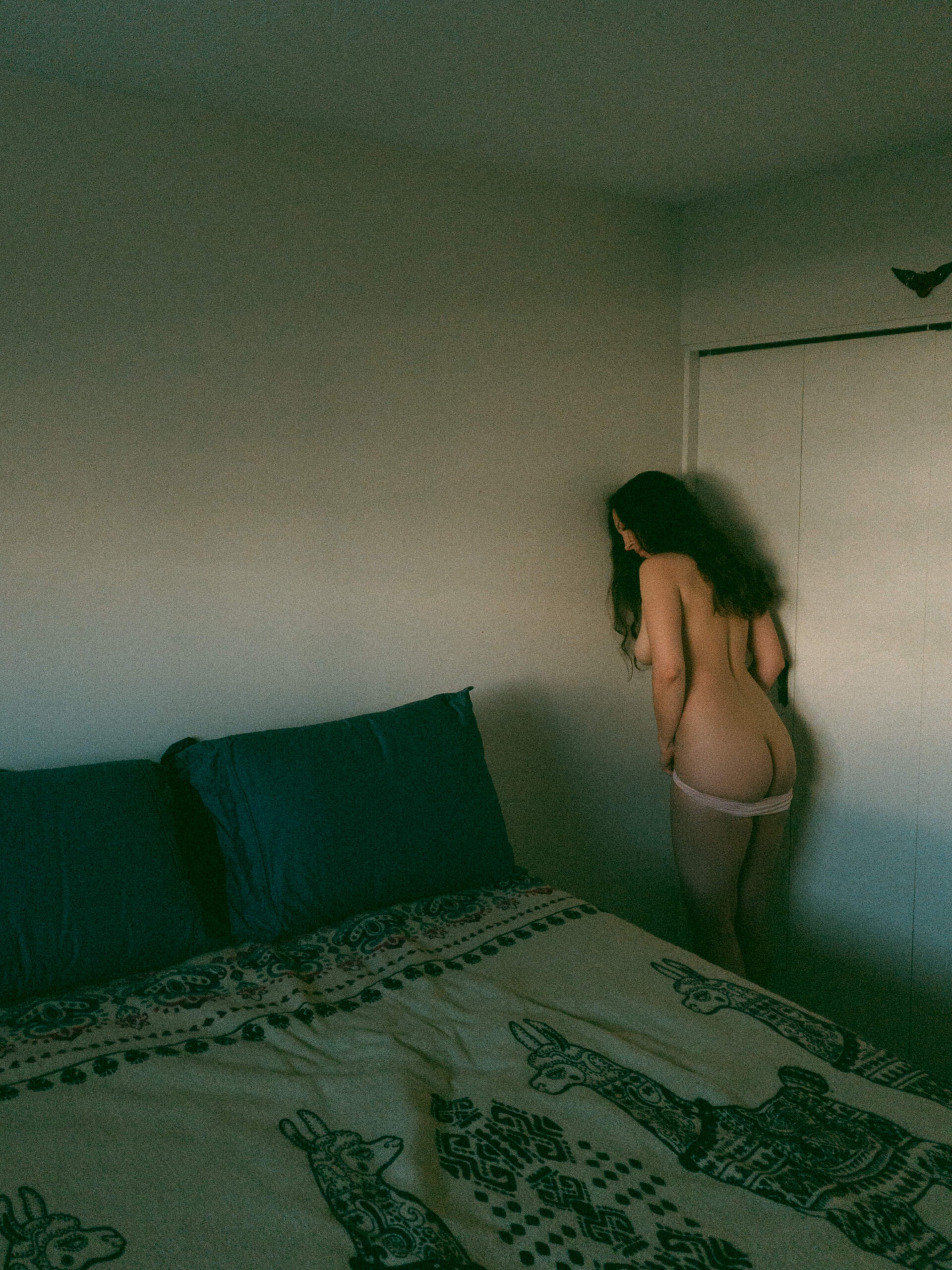 a woman standing by a wall pulling her underwear down during at home boudoir photos 